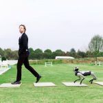 Magicdog EDU Roboterhund folgt elegant gekleidetem Mann draußen auf grüner Wiese